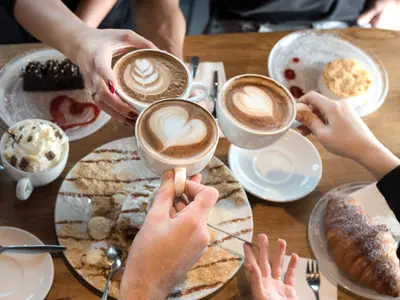 Friends with desserts and coffee, close up.Happy couple sitting around the table. Hands holding cups, happy festive moment, luxury celebration concept.